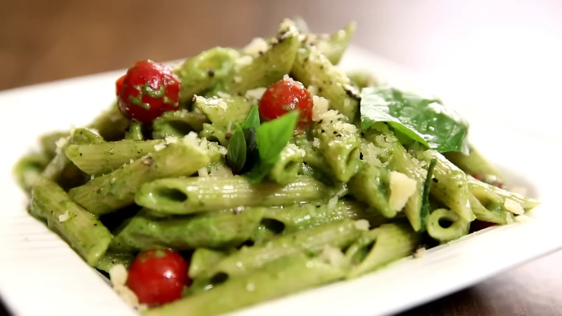 Creamy pesto pasta dish garnished with fresh basil and pine nuts, served in a white bowl on a wooden table.